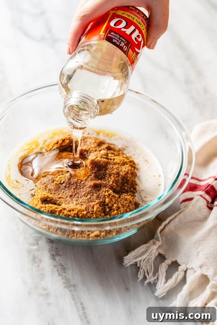 Hand pouring corn syrup into a glass mixing bowl with the ingredients for a cookie crust