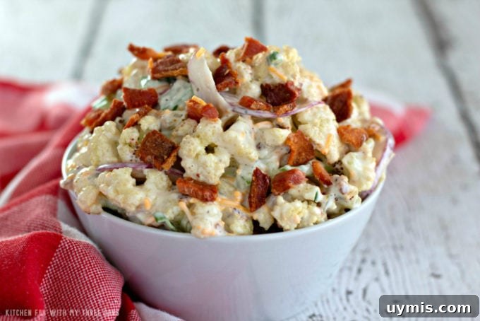 Low Carb Cauliflower Salad in a white bowl on a rustic white table with a red and white check napkin
