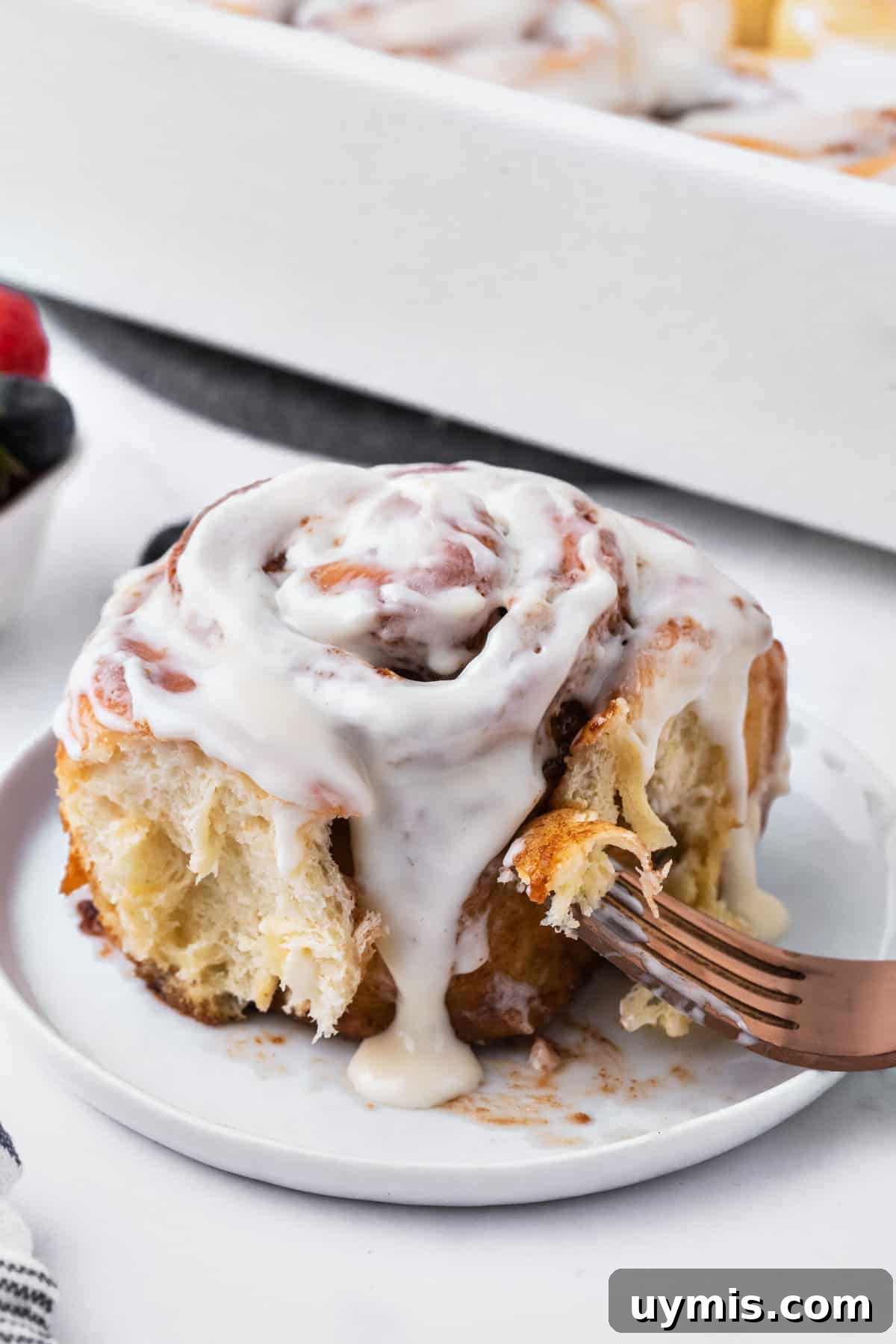 A cinnamon roll is plated with a fork.