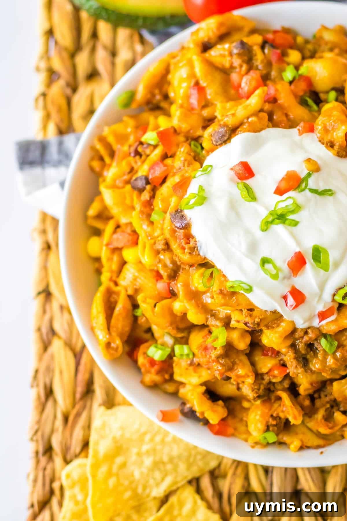 Slow cooker taco pasta topped with sour cream, tomatoes, shredded cheese, and green onions.