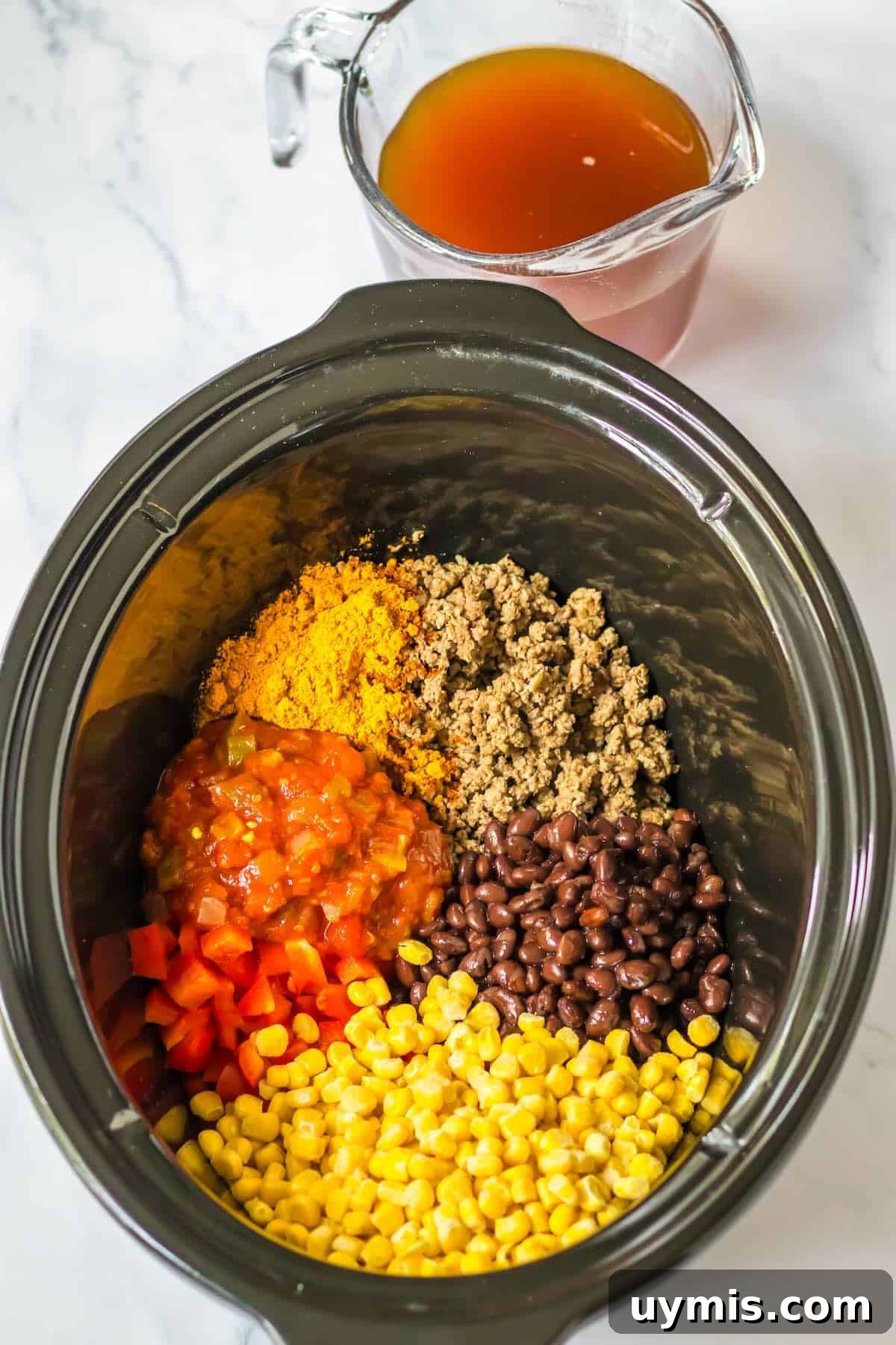 Beef broth being added to ground beef, salsa, corn, black beans, peppers in a slow cooker for taco pasta.