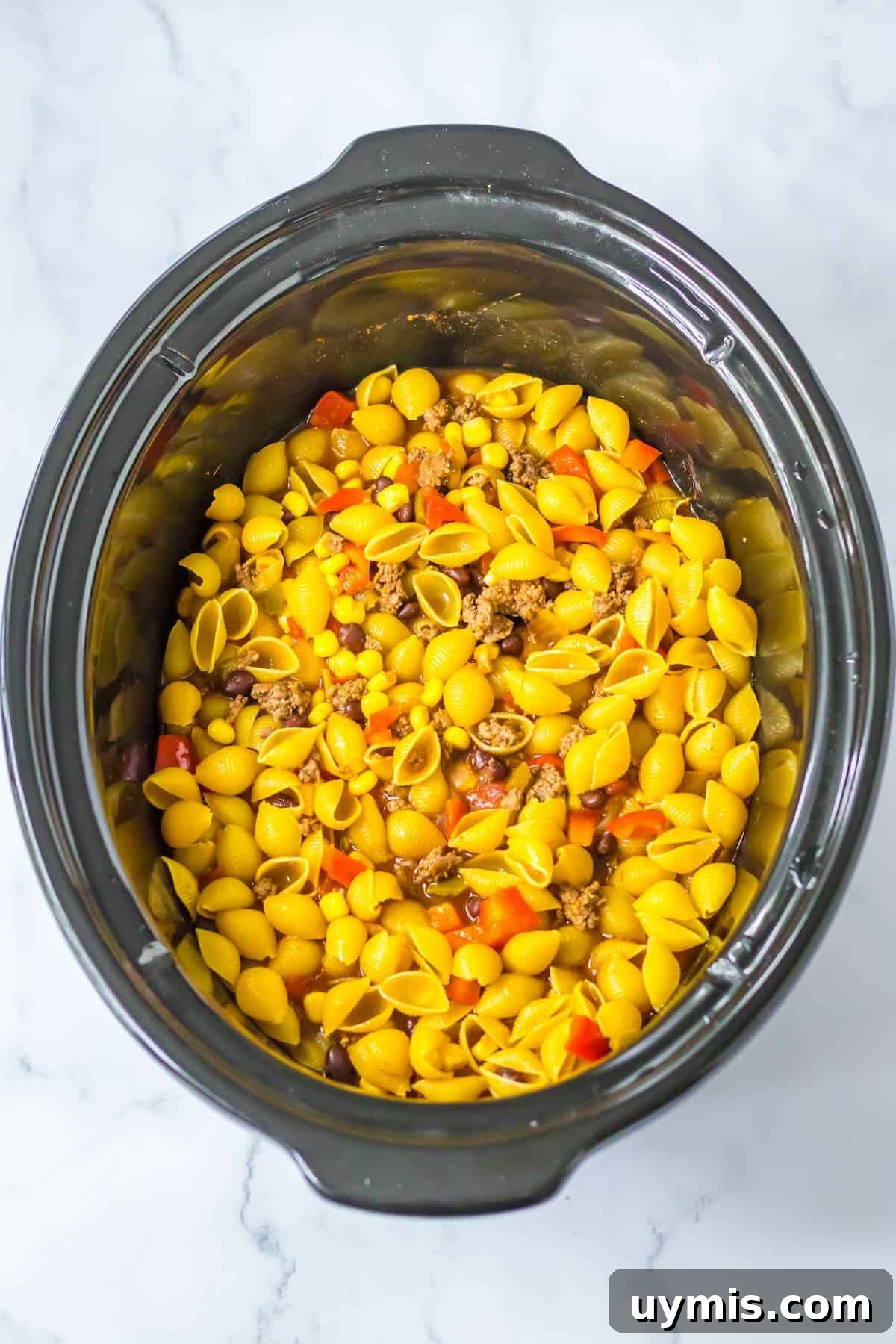 Short pasta being stirred into cheesy taco pasta in the slow cooker.