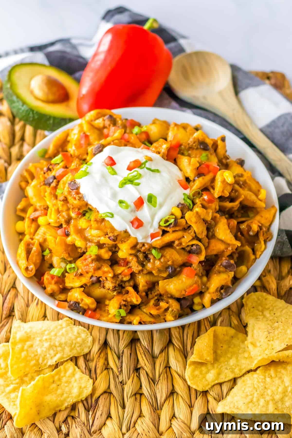Slow cooker taco pasta topped with sour cream, tomatoes, shredded cheese, and green onions.