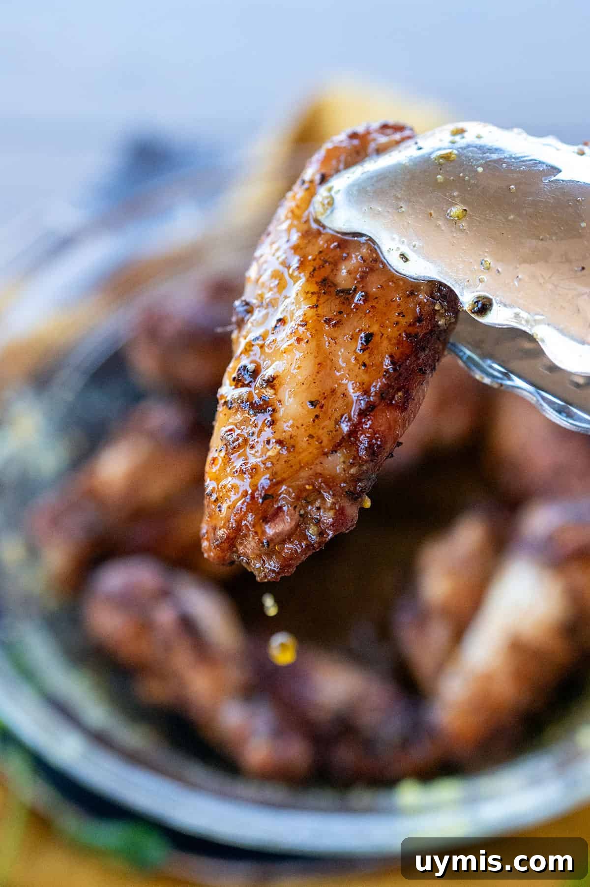Crispy Grilled Lemon Pepper Chicken Wings Recipe 2 Tongs grabbing lemon pepper wings with butter drip.