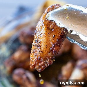Tongs grabbing lemon pepper wings with butter drip.