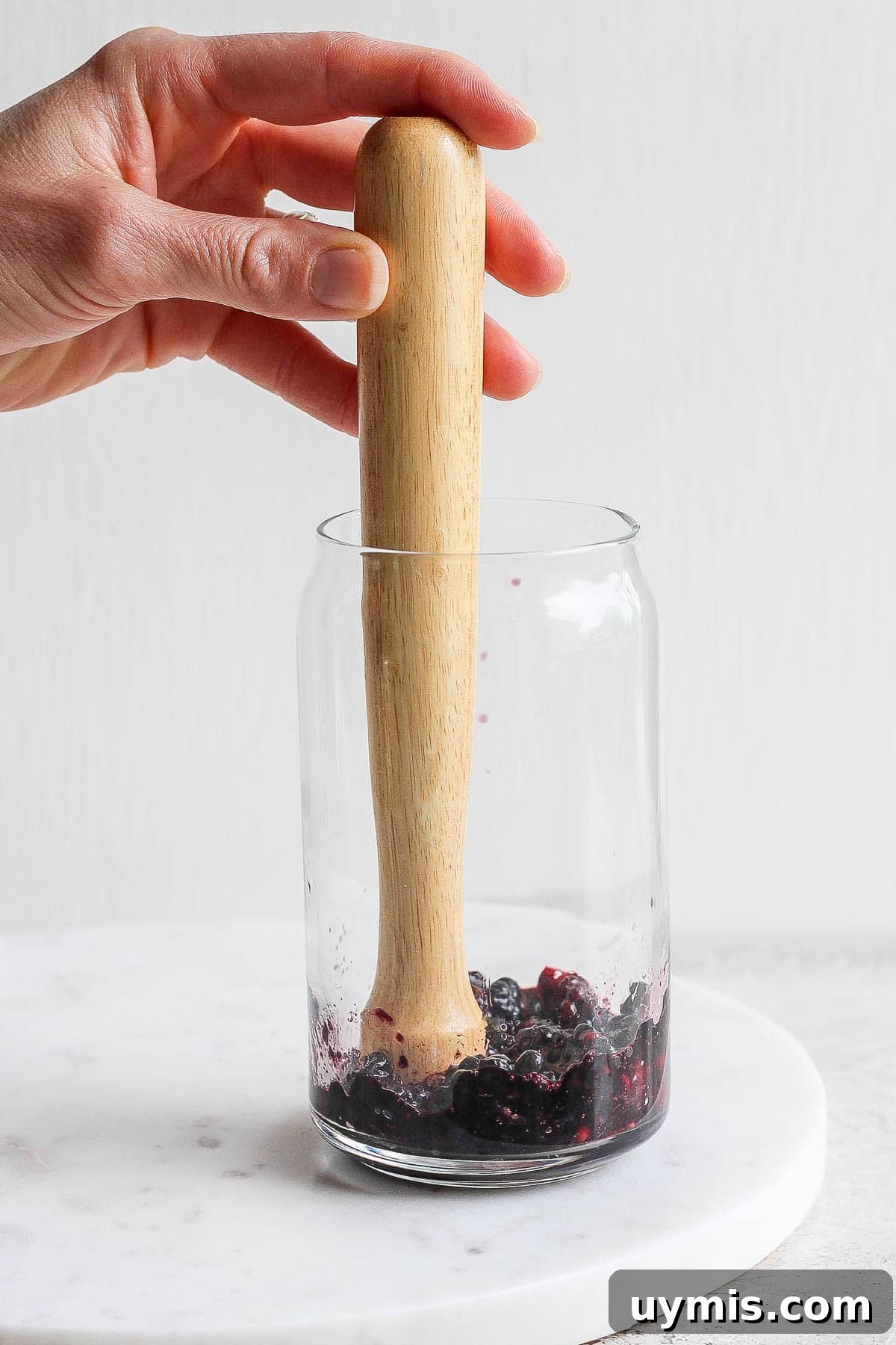 Fresh blackberries being muddled in the bottom of a glass.