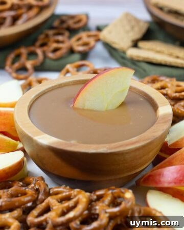 Crunchy Homemade Caramel Corn Recipe from Scratch 5 A bowl of caramel dip in the center of a serving tray with sliced apples and pretzels.