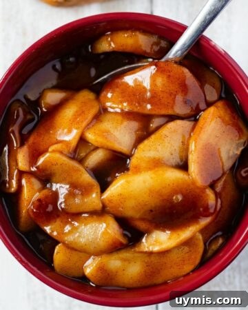 Crunchy Homemade Caramel Corn Recipe from Scratch 8 A brown bowl filled with Instant Pot Cinnamon Apples and a sliced pound cake on a wooden cutting board.