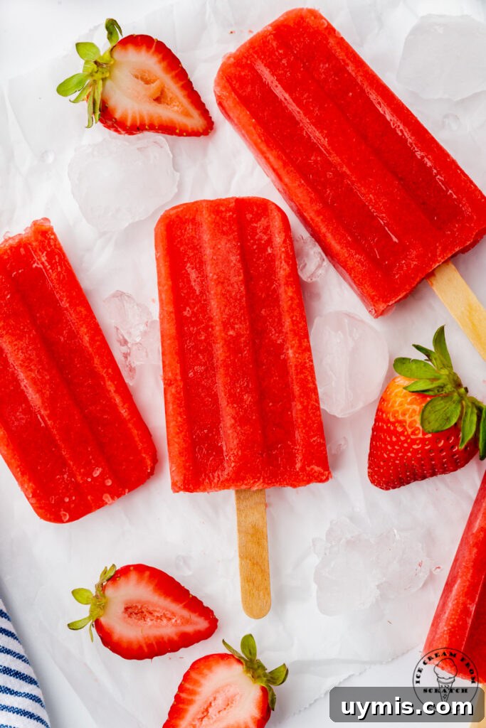 Homemade Fruit Popsicles Recipe for Refreshing Summer Treats 5 three strawberry popsicles on top of ice cubes with halved strawberries, viewed from above.