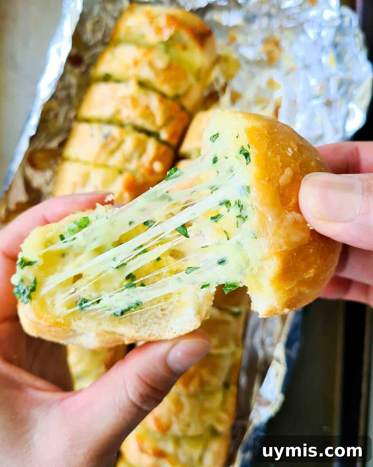 Two slices of freshly baked cheese garlic bread being pulled apart, showing lots of cheese strech