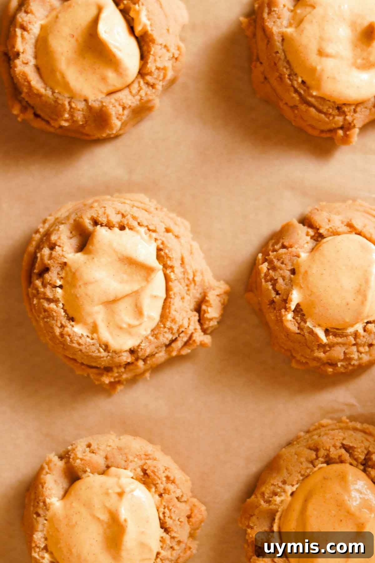Soft Pumpkin Cheesecake Cookies with Cream Cheese Swirl 10 unbaked cookie dough balls on parchment paper with pumpkin filling inside