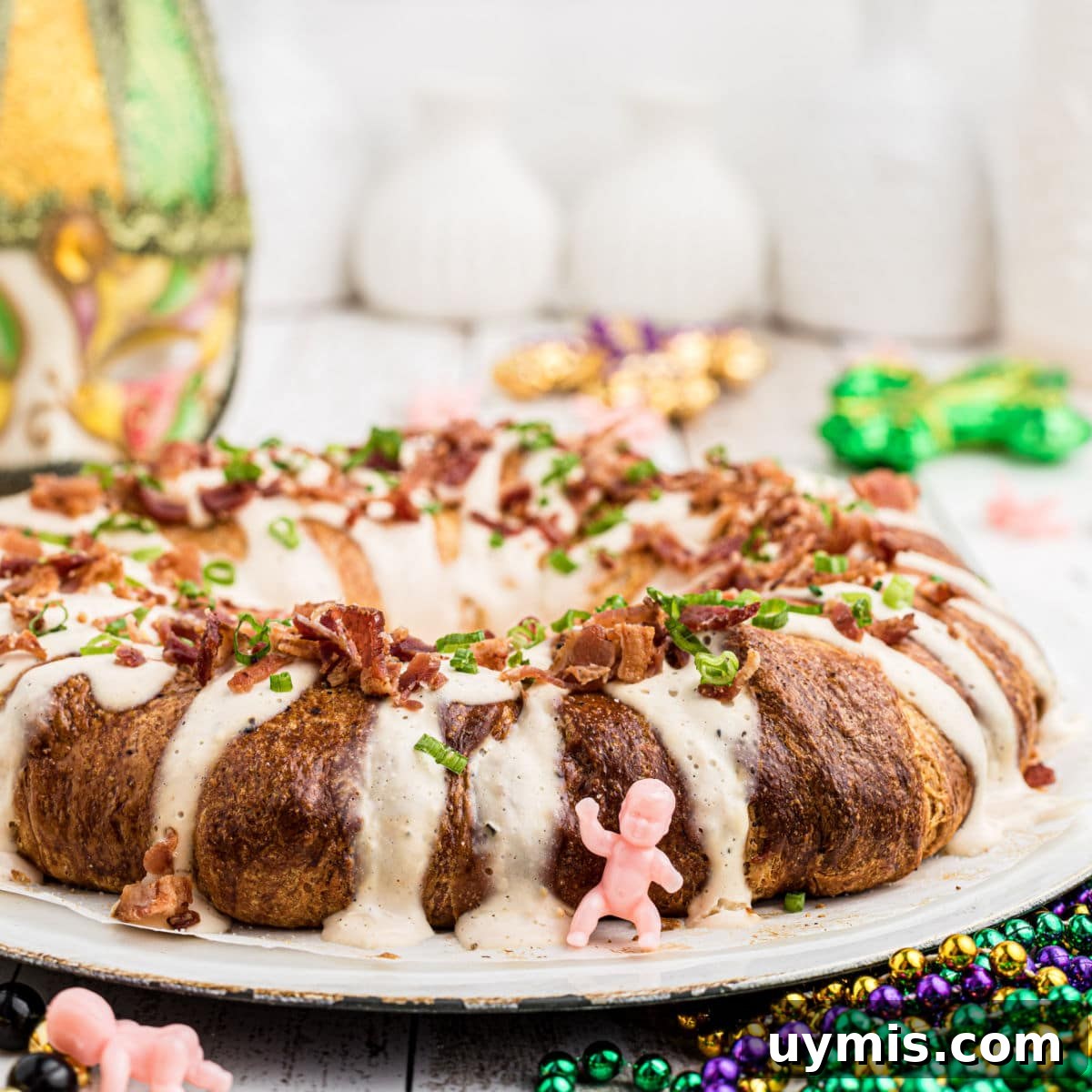 20 Southern Food Blogs to Follow for Classic Comfort Recipes 2 close up from the side of a boudin king cake with a king cake baby in front and some mardi gras stuff in the background