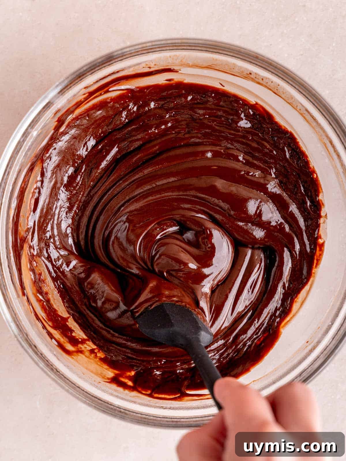 Creamy No-Bake Chocolate Cherry Cheesecake Recipe 8 Stirring silky chocolate ganache in a bowl with a spatula.