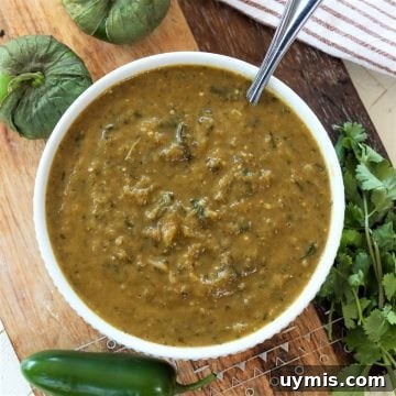 A round white bowl of tomatillo sauce surrounded by peppers and cilantro.