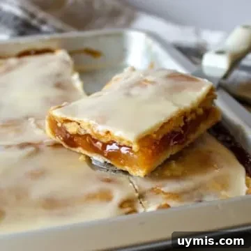 Square apple slice on serving knife above pan of apple slices.