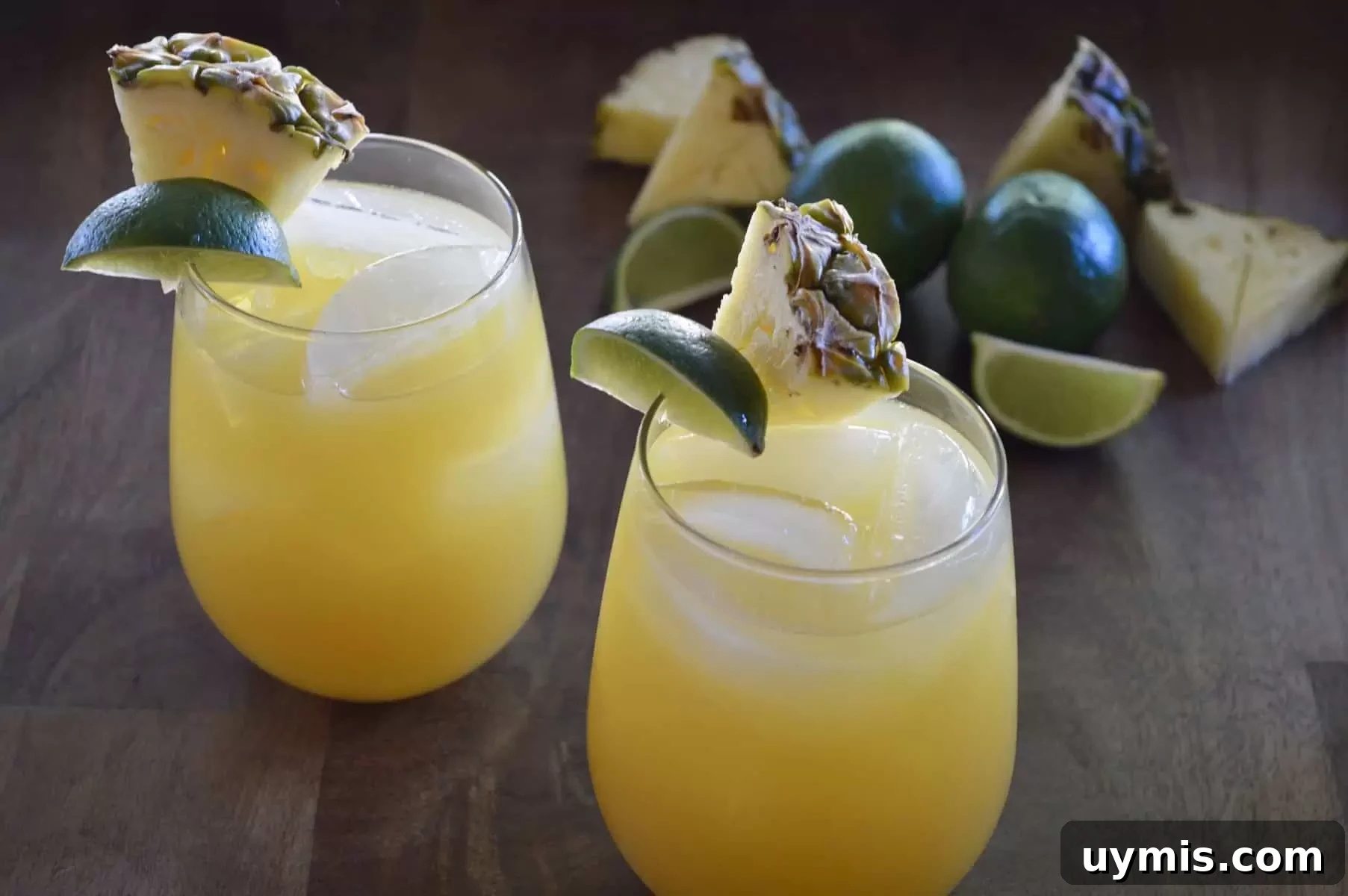 How to Make a Pineapple Margarita Cocktail 2 Pineapple margaritas on a wood platter with pineapples slices and lime wedges.