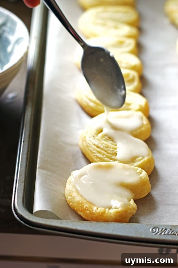 Flaky Heart-Shaped Puff Pastry Recipe 5 Drizzling the glaze with a spoon over the baked puff pastry hearts placed on a baking sheet