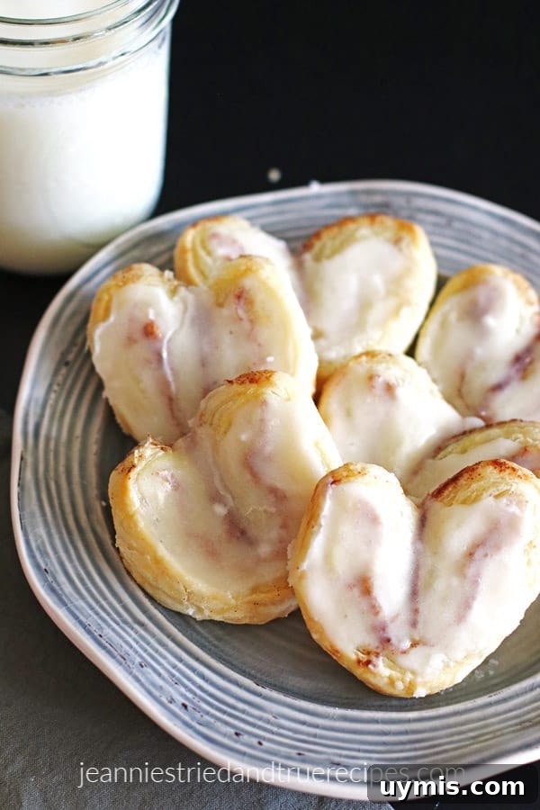 Flaky Heart-Shaped Puff Pastry Recipe 6 Puff Pastry Dessert shaped in hearts with frosting on a grey plate with a glass of milk