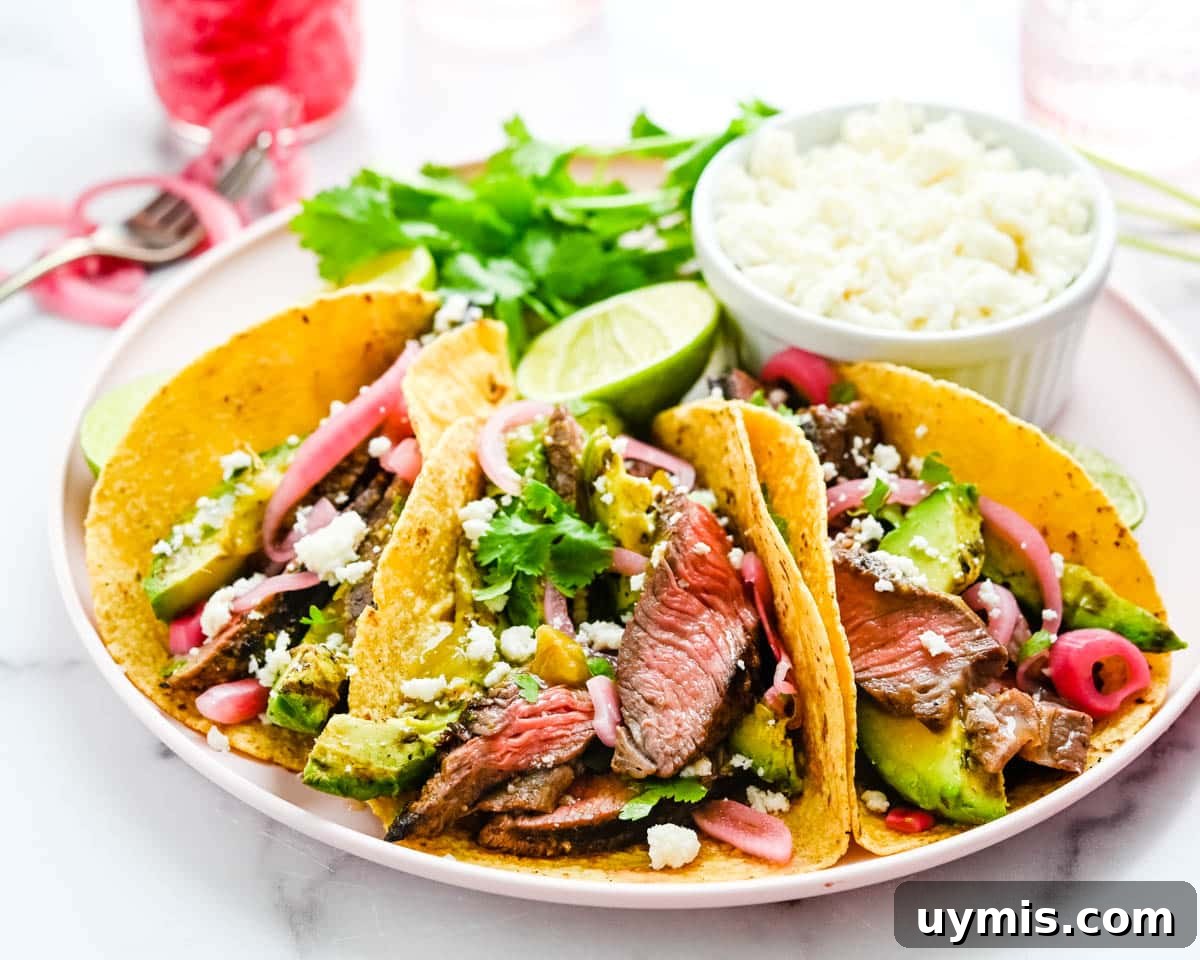 Carne Asada Tacos with Juicy Grilled Steak 12 A plate of dressed grilled steak tacos on corn tortillas with grilled avocado and pickled red onion.