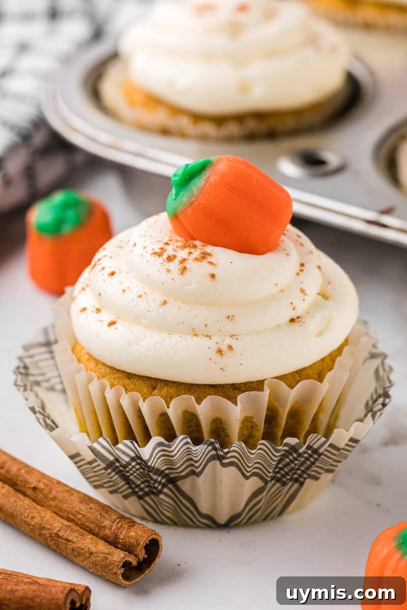 Moist Pumpkin Cupcakes with Cinnamon Cream Cheese Frosting 2 closeup of a pumpkin cupcake topped with buttercream frosting and a pumpkin candy.