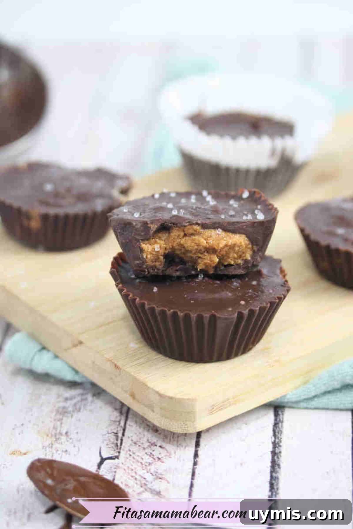 High-Protein Almond Butter Dark Chocolate Cups 8 Two almond butter protein cups stacked with the top having a bite out of it on a wooden cutting board.
