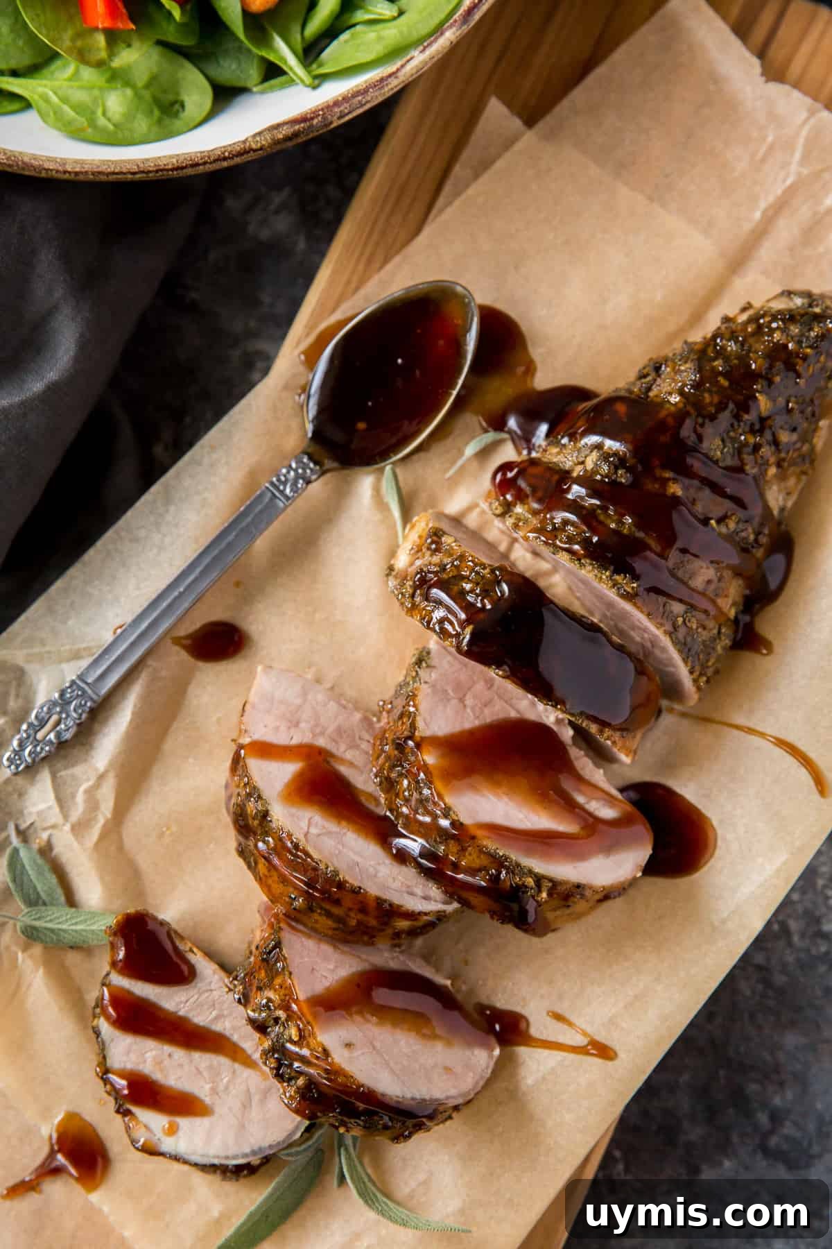 Balsamic Glazed Pork Tenderloin Recipe 3 Sliced pork tenderloin on parchment paper next to a bowl of green salad.
