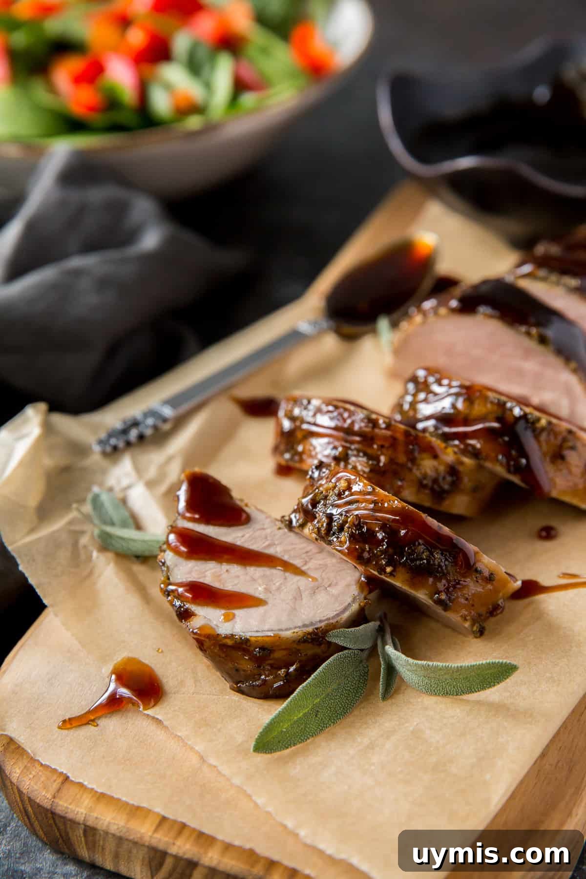 Balsamic Glazed Pork Tenderloin Recipe 6 Sliced pork tenderloin on parchment paper next to a bowl of green salad.