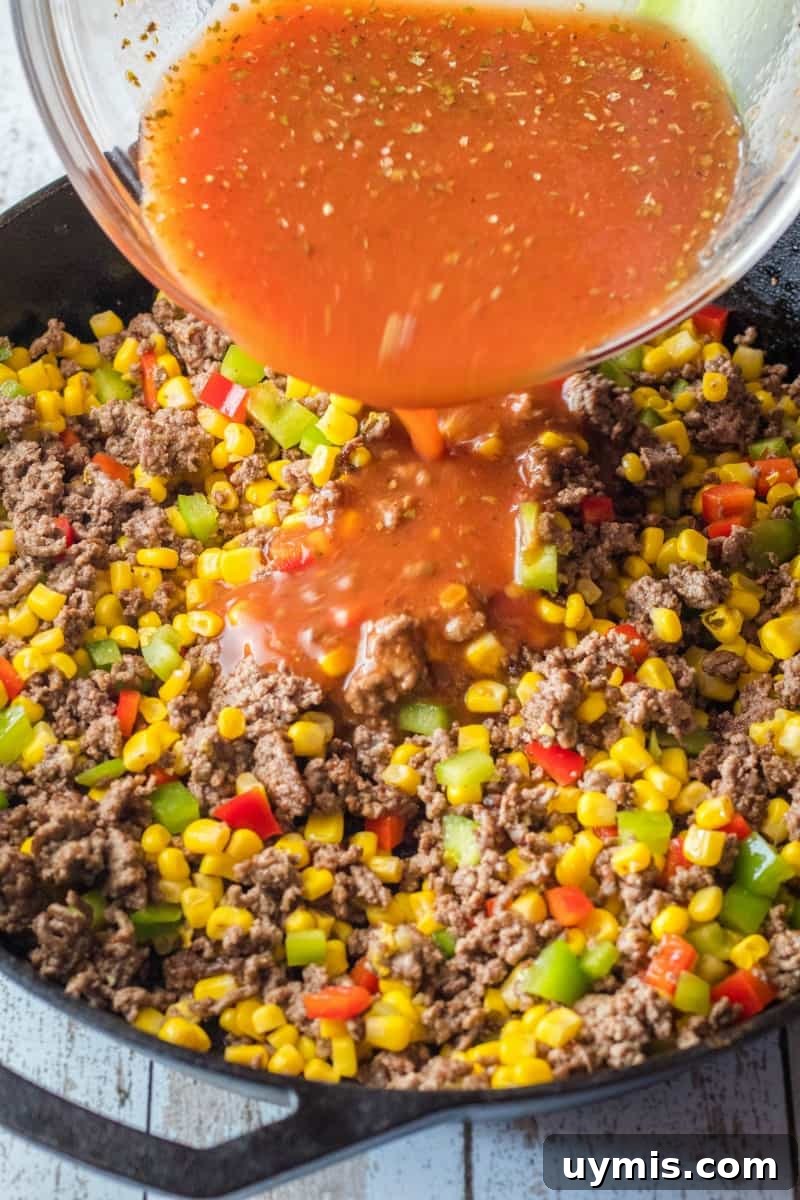 sloppy joe sauce being poured over ground beef and veggies
