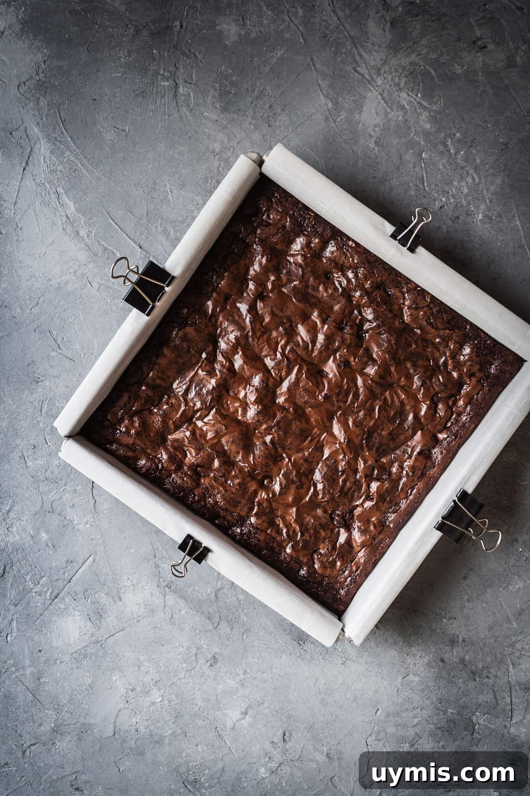 Chocolate Brownies with Port-Soaked Cherries 4 Overhead view of a square pan of brownies with port soaked cherries on a grey background