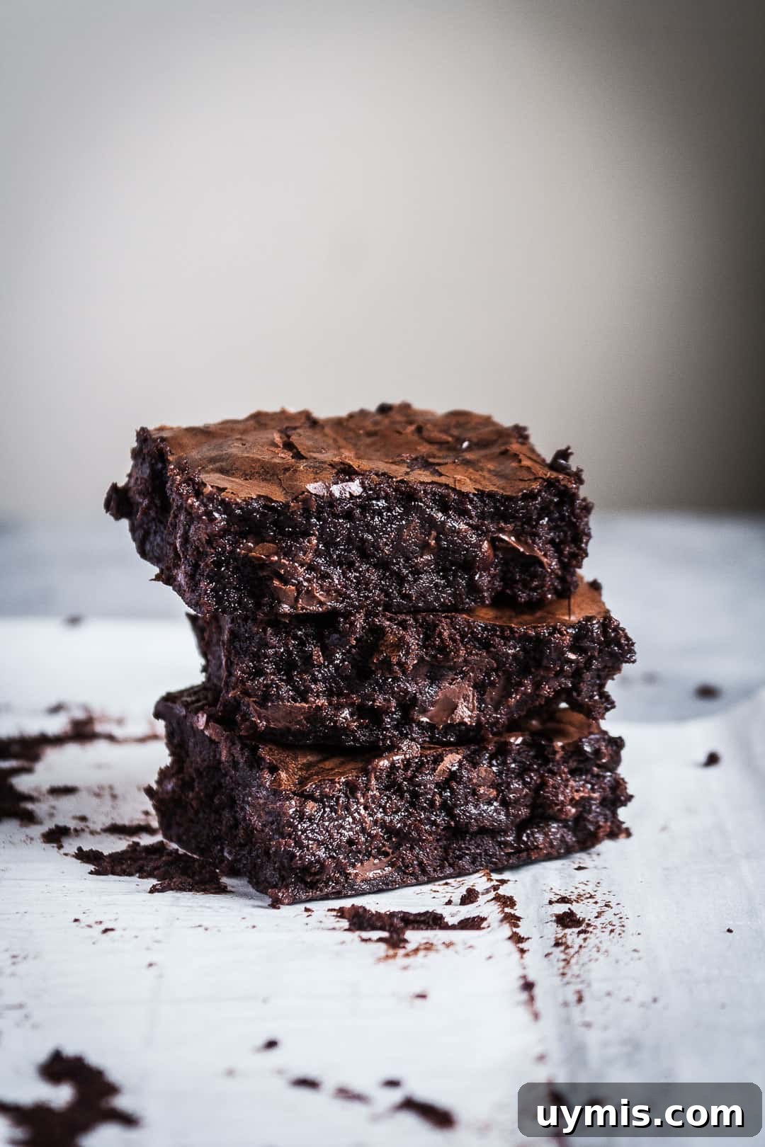 Chocolate Brownies with Port-Soaked Cherries 5 Side view close up of three squares of brownies with port soaked cherries stacked in a tower on parchment paper and a grey background