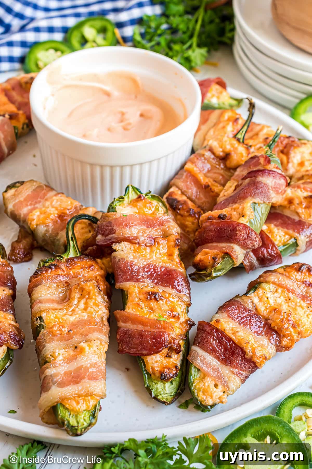 Bacon wrapped jalapenos on a white plate with a bowl of dip.