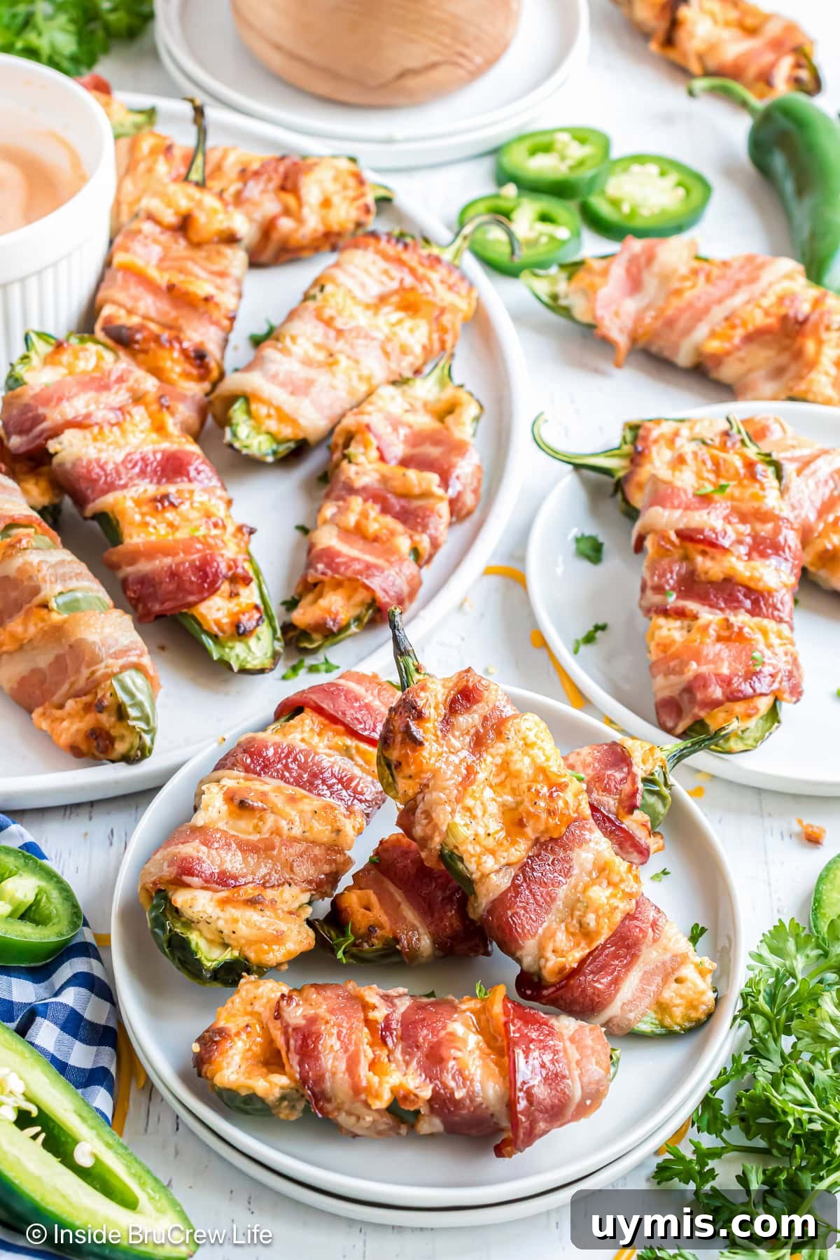 A table covered with white plates filled with bacon wrapped jalapeno poppers.