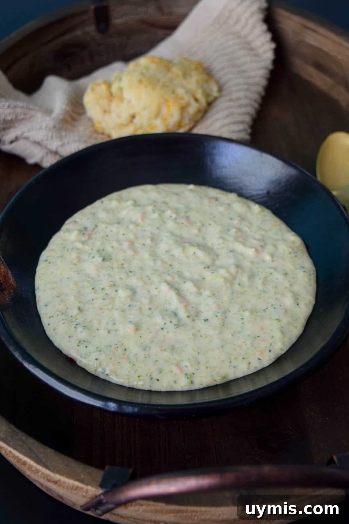 Creamy Homemade Broccoli Cheddar Soup Recipe 8 The Best Broccoli Cheddar Soup in black bowl with biscuit behind bowl on brown napkin close up view