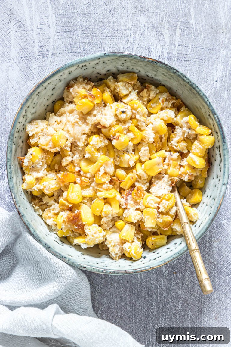 Creamy Scalloped Corn Casserole Recipe 3 a serving of scalloped corn in a blue bowl with a gold spoon