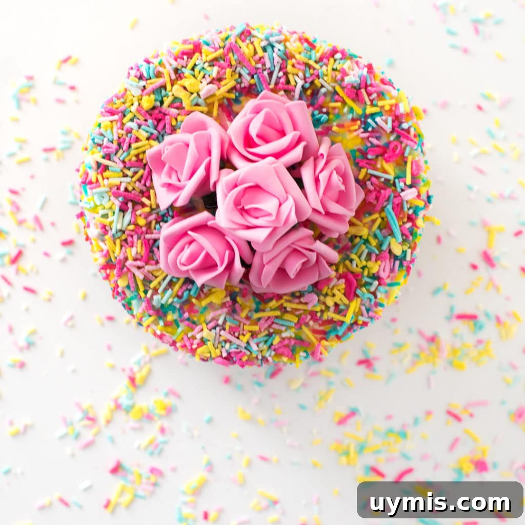 Keto Sugar Free Birthday Cake Everyone Will Love 7 Overhead photo of a cake coated in sprinkles with pink flowers on top.