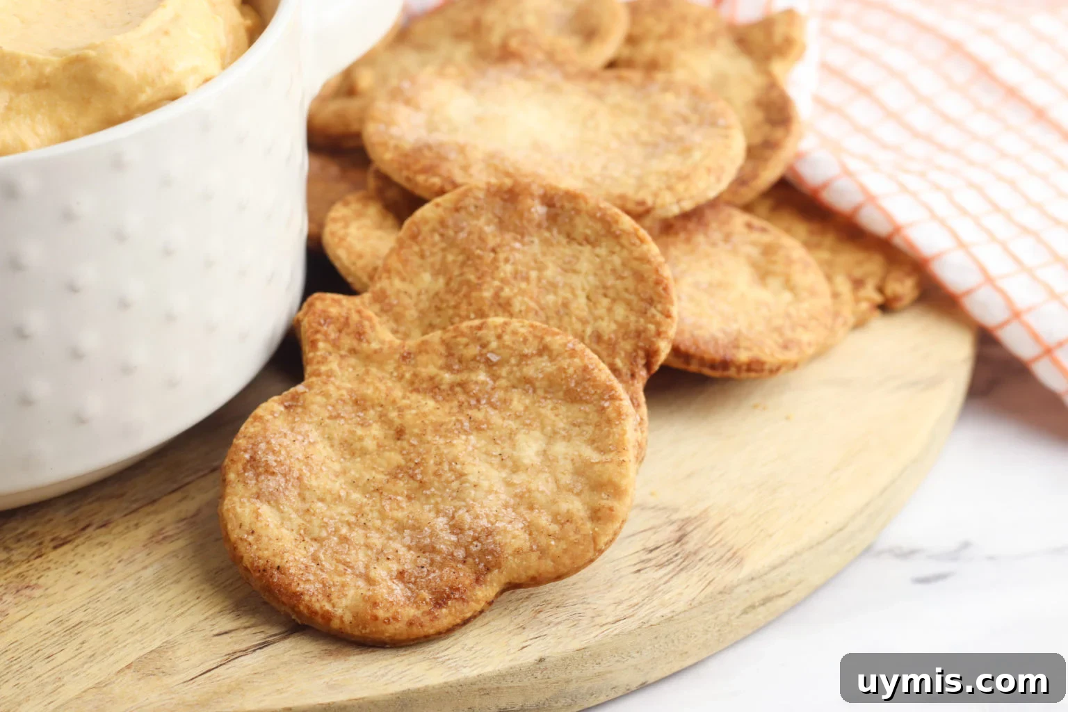 Flaky Pie Crust Crackers Recipe 3 Pie Crust Crackers on a wooden cutting board with a crock of dip on the side.