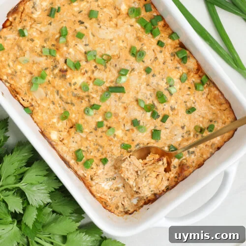 Creamy buffalo chicken dip baked in a white dish and topped with chopped green onions, served hot and ready for dipping.