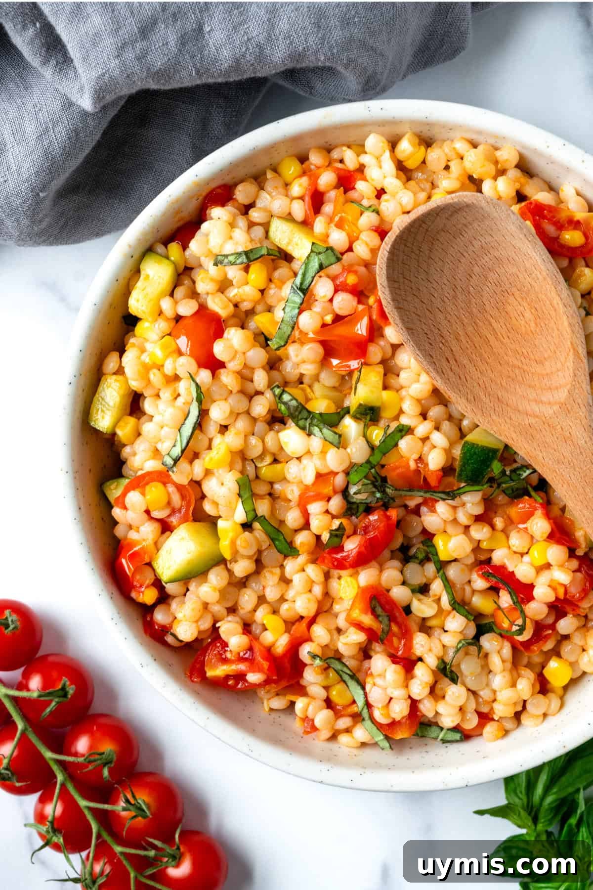Zesty Summer Couscous Salad with Fresh Herbs 6 Summer Couscous Salad in a white bowl with a wooden serving spoon.