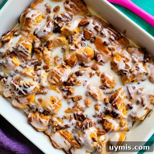 Overhead shot of the baked cinnamon roll breakfast casserole, maple syrup and icing drizzled, ready for serving at a holiday brunch table.