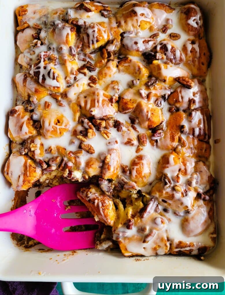 Cinnamon roll breakfast casserole baked in a 9×13-inch dish with golden brown top, drizzled with maple syrup, icing, and sprinkled pecans.