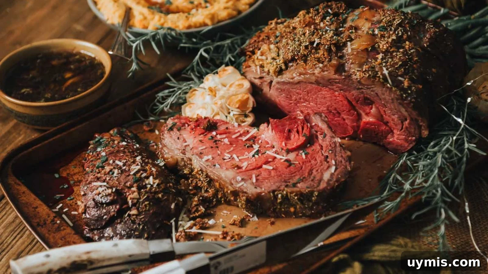 21 Elegant Easter Main Courses for a Stunning Holiday Table 2 Sliced roasted beef on a tray, surrounded by herbs and a whole head of roasted garlic, with a bowl of sauce in the background.