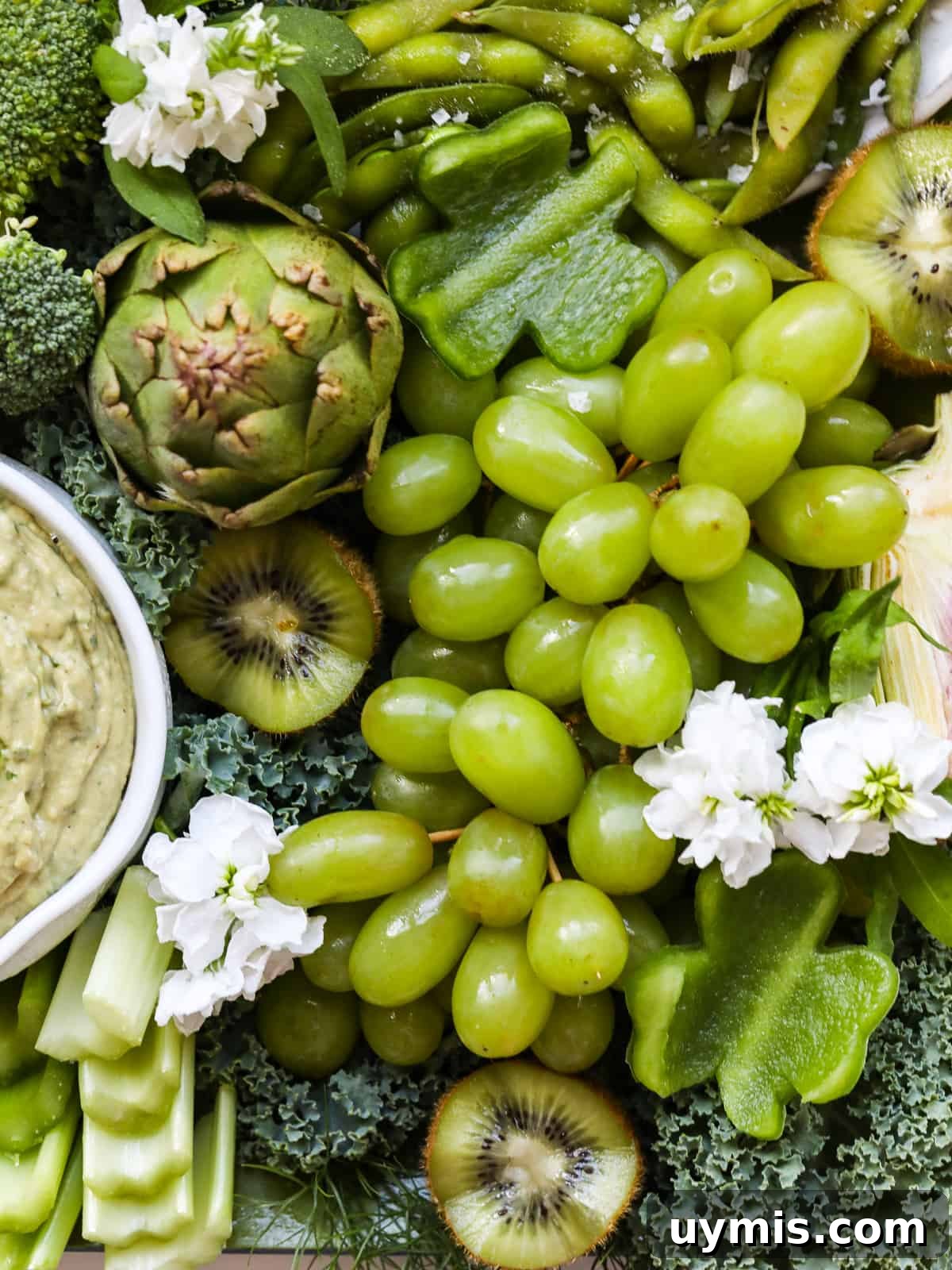 St. Patrick's Day Green Snack Ideas for Parties 3 Shiny green grapes, shamrock shaped pieces of bell pepper and more green vegetables on a snack tray with a green dip.