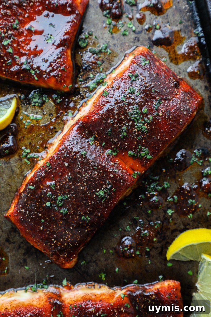 Oven-Baked Brown Sugar-Spiced Salmon 6 A piece of baked sugar spiced salmon sitting on a dark metal tray sprinkled with chopped parsley and surrounded by lemon wedges
