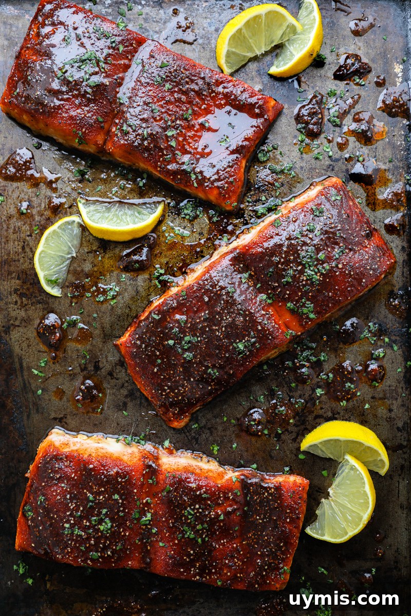 Oven-Baked Brown Sugar-Spiced Salmon 8 3 baked sugar spiced salmon fillets sitting on a dark metal tray next to fresh lemon wedges