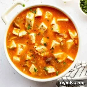 Soft tofu chunks in a bright orange-red sauce in a white pot.