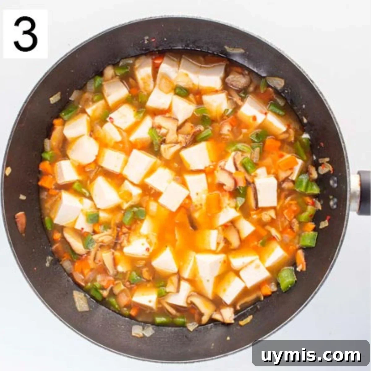 Quick Spicy Silken Tofu Recipe with Garlic Chili Sauce 6 Chunks of white tofu and chopped vegetables in orange liquid in a skillet.