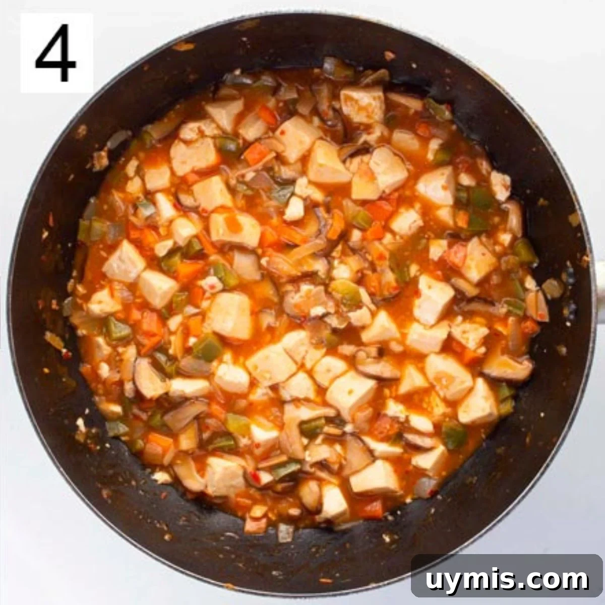 Quick Spicy Silken Tofu Recipe with Garlic Chili Sauce 7 Chunks of white tofu and mixed vegetables in a thick orange sauce in a pan.