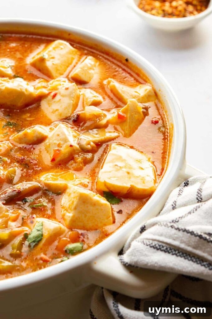 Quick Spicy Silken Tofu Recipe with Garlic Chili Sauce 8 Close up of silken tofu floating in a thick orange-red sauce with vegetables.