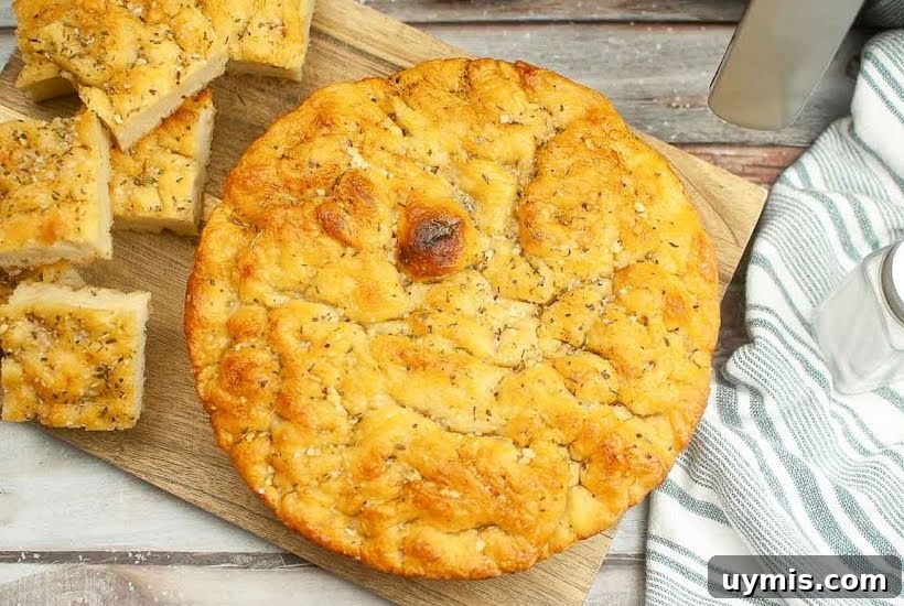 Crispy Air Fryer Focaccia Bread Recipe 8 Overhead view of a round of homemade focaccia on a cutting board, with sliced bread on the left.