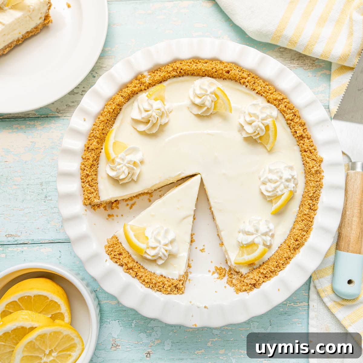 Lemon Icebox Pie Recipe with Creamy No Bake Filling 8 A lemon cream pie with a graham cracker crust, decorated with whipped cream and lemon slices, with one slice removed and placed on a plate.